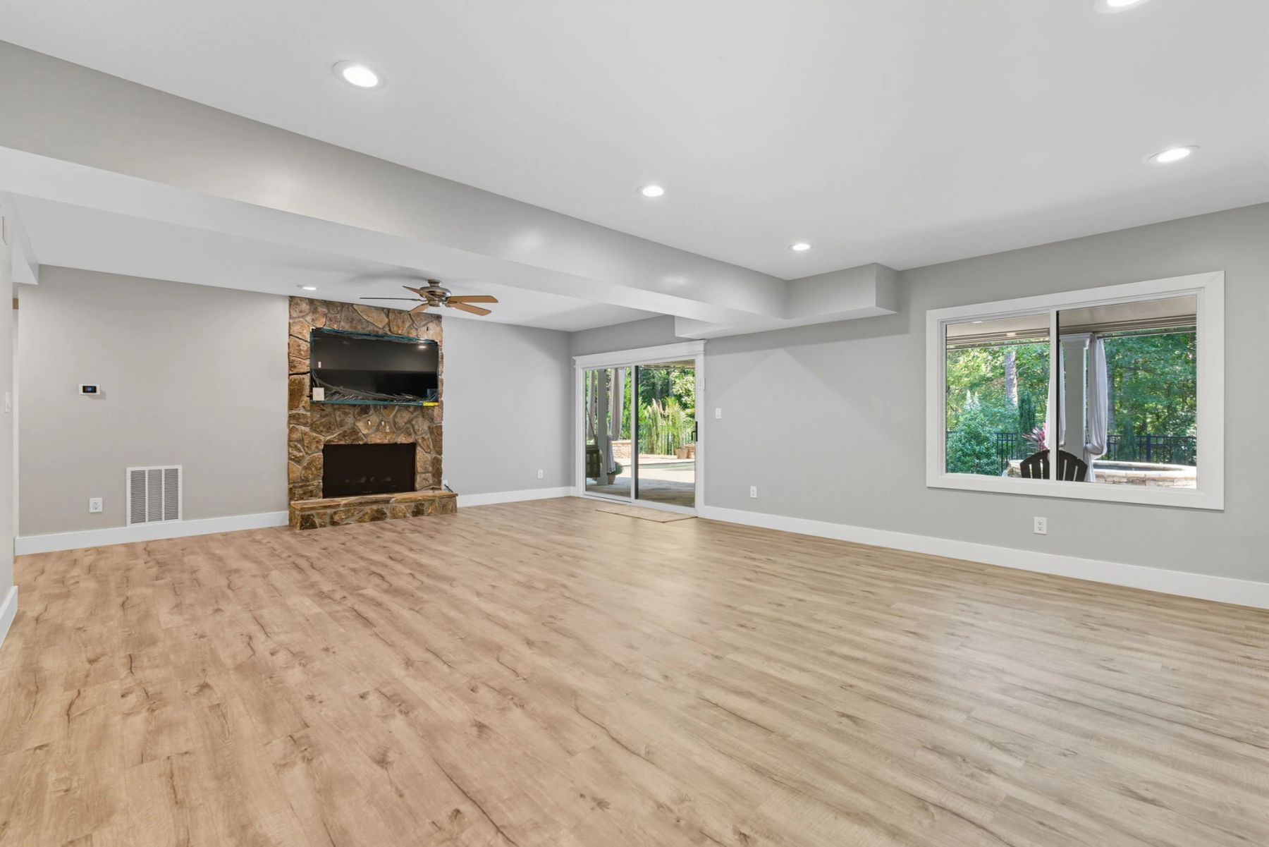 Finished walkout basement with a stone fireplace, recessed lighting and wide wood-look flooring