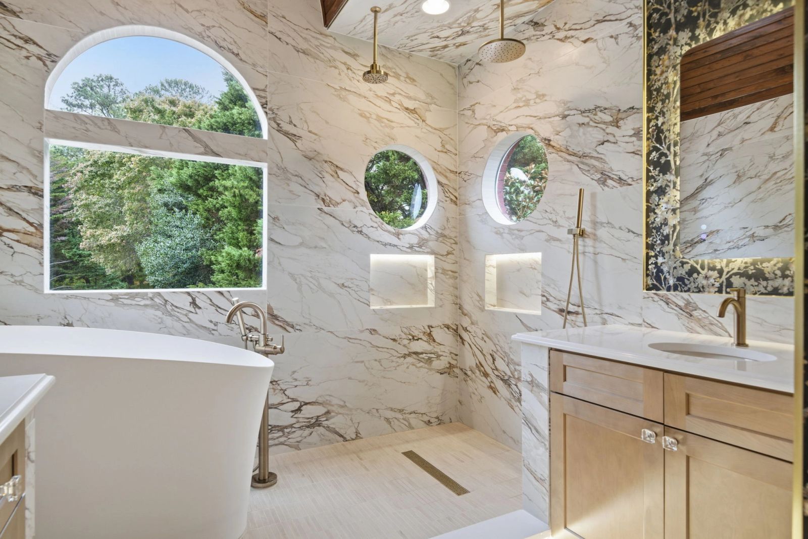 Marble-pattern bathroom with a freestanding tub, arched window, circular windows and brass fixtures