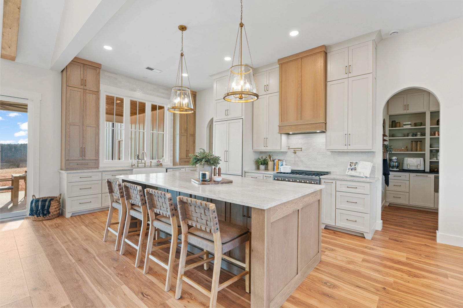 Expansive kitchen with a large wood island, stone countertop, brass pendants and an arched pantry entrance
